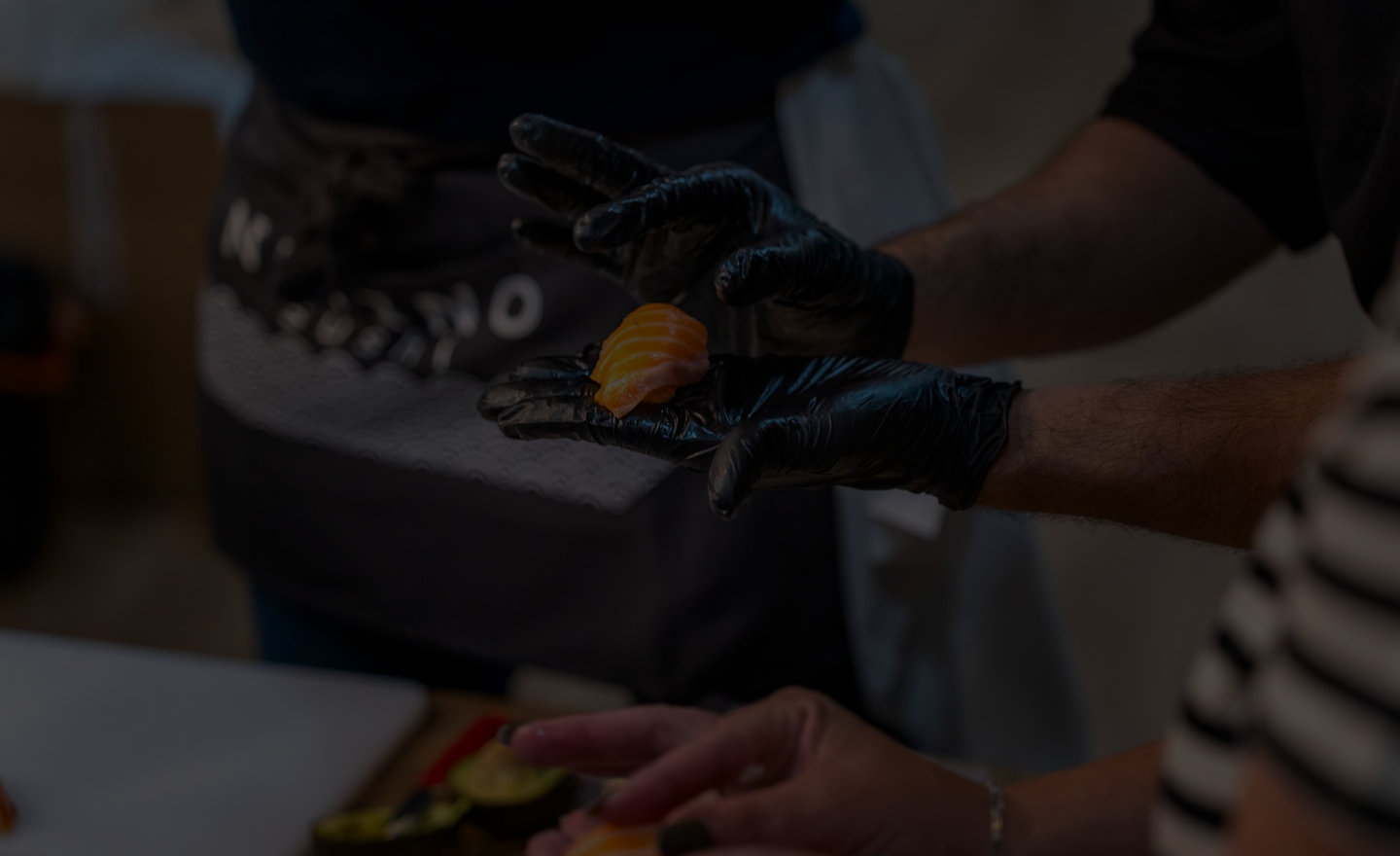 A cocktail and premium sushi dishes staged on a dramatic black table.
