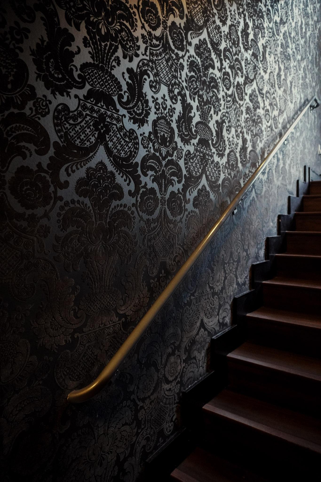 Damask-wallpapered staircase with a gold handrail inside Tokyo Sushi Speakeasy.