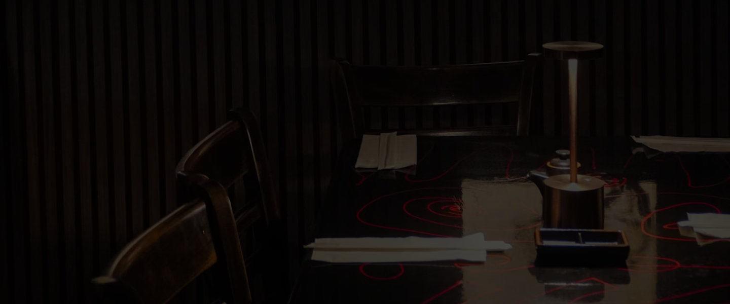 A moody table setting inside Tokyo Sushi Speakeasy with Japanese scroll art and dark slatted walls.